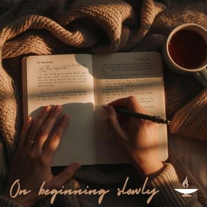 Pictured is a cozy setting with a journal on top of a blanket with hands holding a pen in the right hand and a coffee cup to the right of the the journal, all with sunlight coming through a window from the right