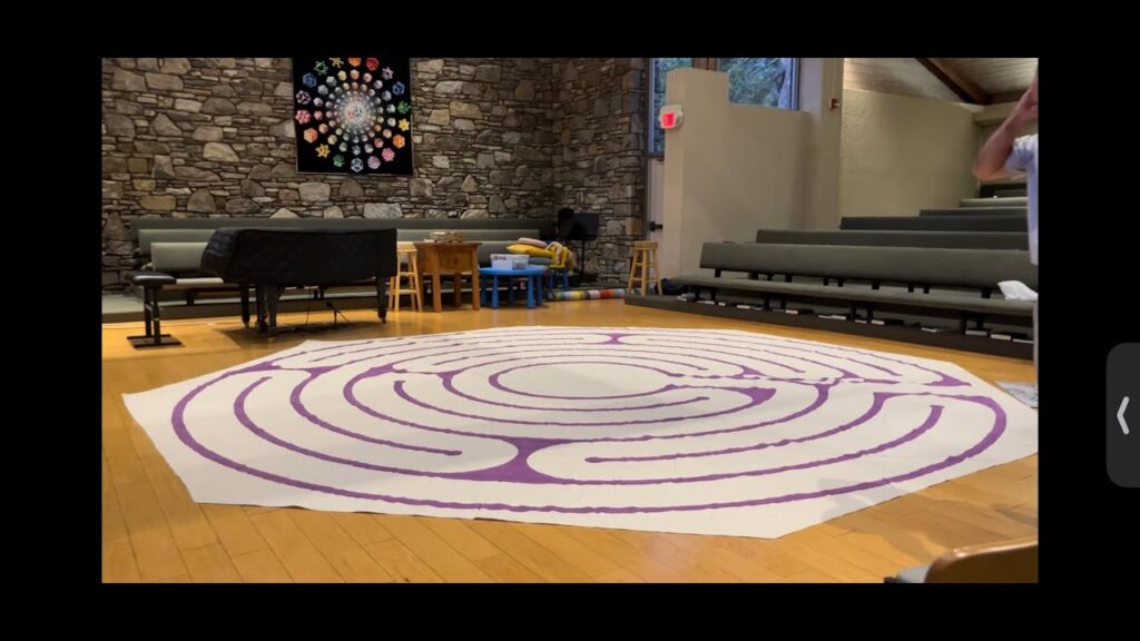The image shows a fabric labyrinth laid out on the floor of the UU AVL Sanctuary next to a grand piano