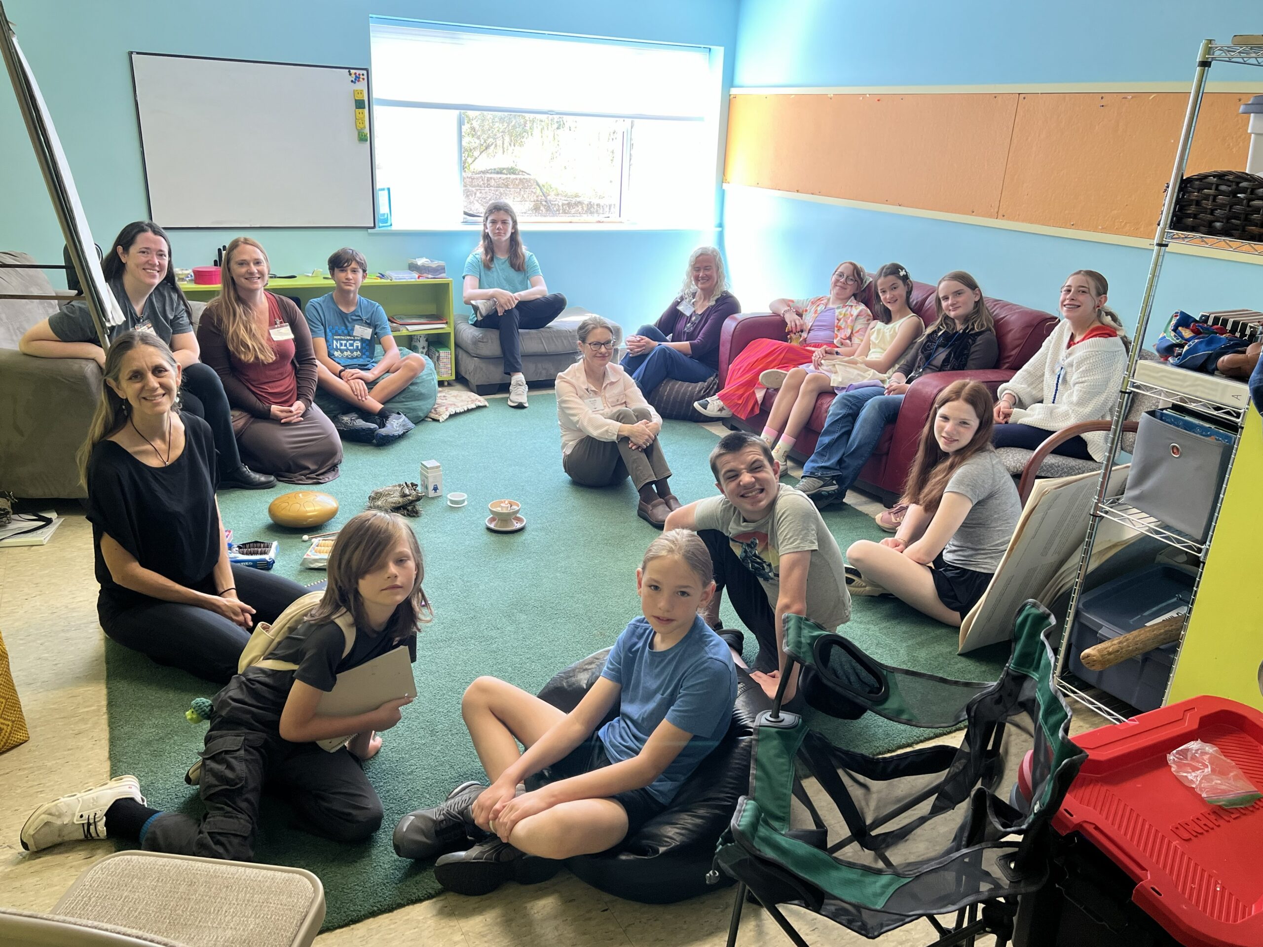 a group of UU Asheville youth and adults sit together in a classroom, and all have turned to look toward the camera to smile